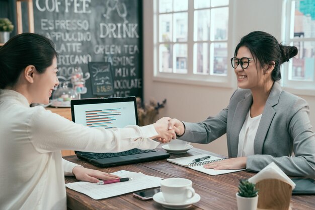 retrato de empresários de mulher asiática apertando as mãos terminando reunião café. corretor de seguro de hipoteca agente consultor financeiro sorrindo para o cliente no café. duas senhoras fazem acordo de acordo