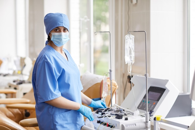 Retrato de enfermeira com máscara e uniforme enquanto trabalhava com equipamentos médicos para doação de sangue em hospital