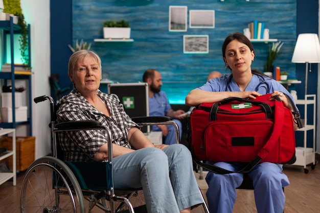 Retrato de enfermeira especializada em atendimento a idosos e aposentada em cadeira de rodas. profissional de saúde segurando um saco de instrumentos médicos para verificar o paciente idoso.