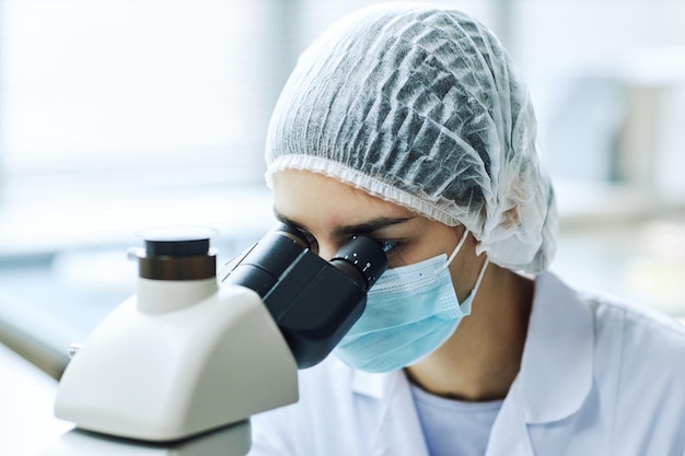 Retrato de engenheira biológica feminina olhando no microscópio enquanto trabalhava em laboratório científico