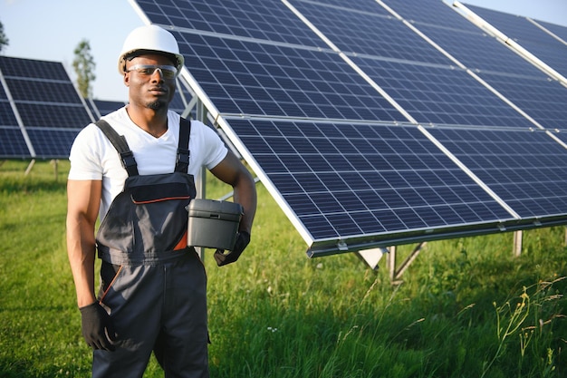 Retrato de engenheiro eletricista afro-americano em capacete de segurança e uniforme instalando painéis solares