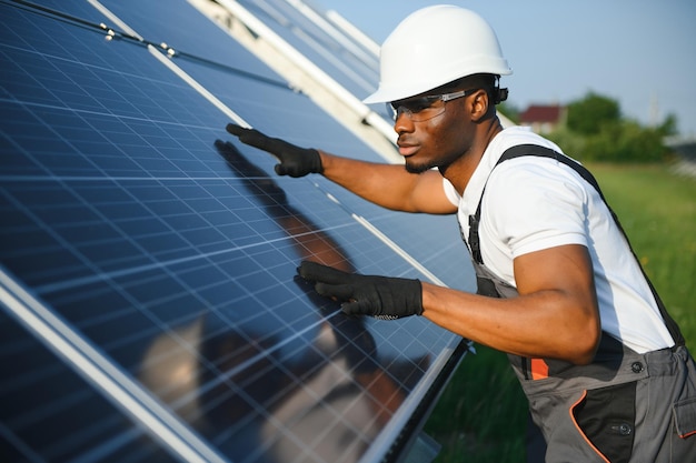 Retrato de engenheiro eletricista afro-americano em capacete de segurança e uniforme instalando painéis solares