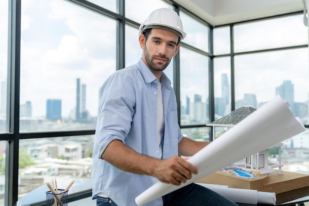 Foto retrato de engenheiro olhando para a câmera enquanto lê o traçado do plano do projeto