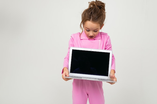 Retrato de engraçadinha encantadora em traje rosa, mostrando a tela do laptop