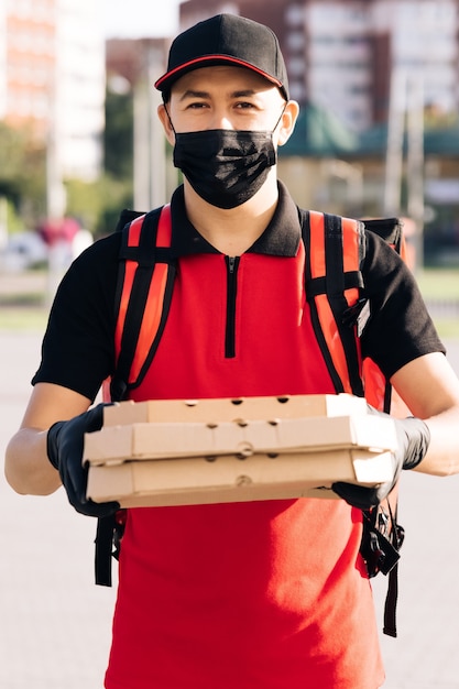 Retrato de entregador de correio com mochila vermelha segurando pizza em caixas de papelão