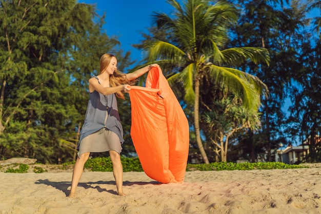 Retrato de estilo de vida de verão da mulher infla um sofá laranja inflável na praia da ilha tropical Relaxando e curtindo a vida na cama de ar