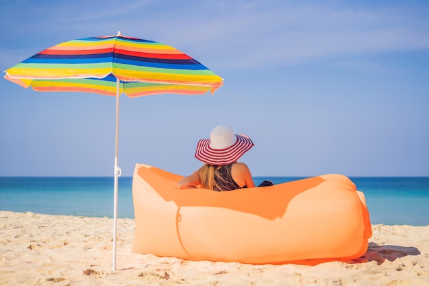 Retrato de estilo de vida de verão de menina bonita sentada no sofá inflável laranja na praia da ilha tropical Relaxando e curtindo a vida na cama de ar