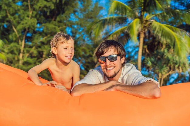 Retrato de estilo de vida de verão de pai e filho sentado no sofá inflável laranja na praia da ilha tropical Relaxando e curtindo a vida na cama de ar