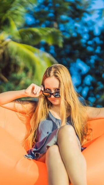 Retrato de estilo de vida de verão de uma menina bonita sentada no sofá inflável laranja na praia de