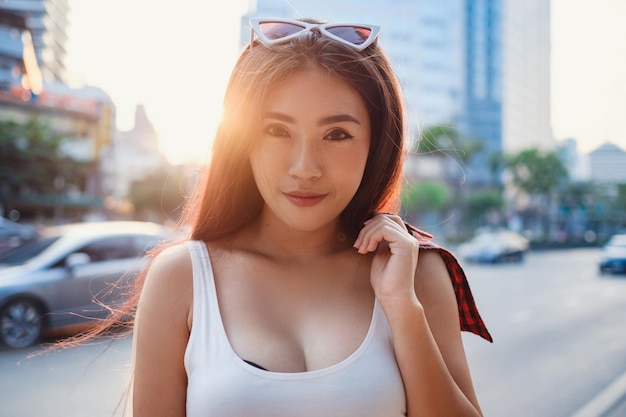Retrato de estilo de vida ensolarado de verão de uma jovem elegante hipster andando na rua vestindo roupas bonitas da moda Viajante turístico de jovens mulheres asiáticas sorrindo na moda de rua de bangkok