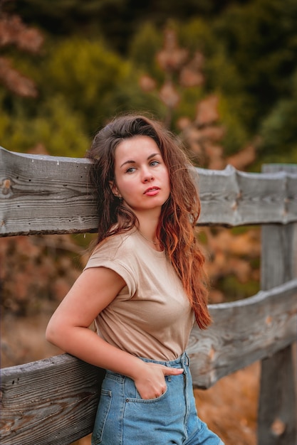 Retrato de estilo rural de uma jovem encostada a uma cerca de madeira na aldeia no início do outono