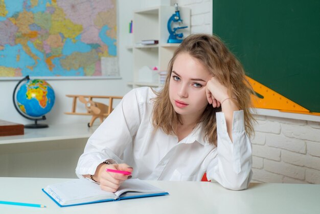Retrato de estudante adolescente de uma jovem pensativa fazendo anotações enquanto está sentado com livros