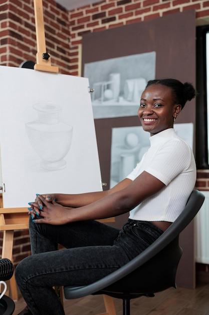 Retrato de estudante afro-americano participando da aula de arte aproveitando a aula de desenho no estúdio de criatividade. Mulher pintor modelo de vaso de desenho em tela branca, trabalhando na técnica gráfica. Conceito criativo