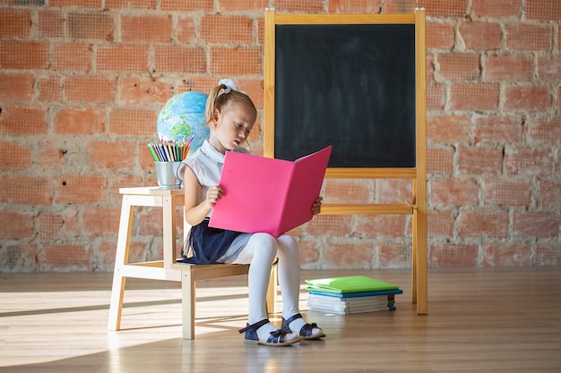 Retrato de estudante caucasiana lendo um livro na frente do quadro-negro, de volta ao conceito de escola