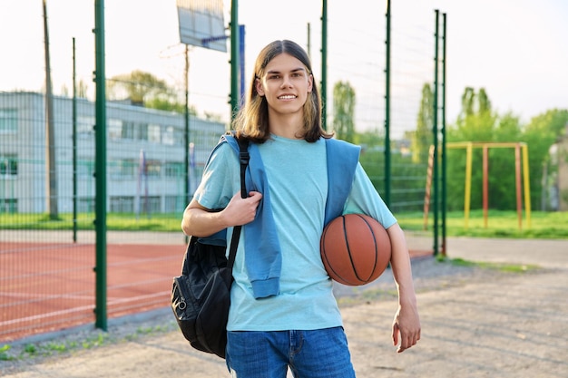 Retrato de estudante com bola de mochila perto do playground de basquete ao ar livre