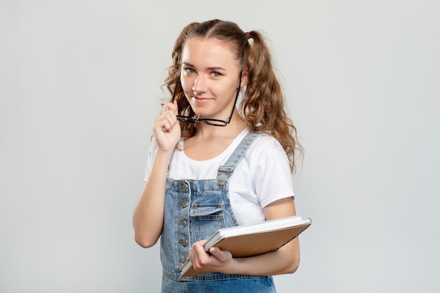 Retrato de estudante confiante Vida escolar Adolescente inteligente alegre com livros tirando óculos sorrindo isolado no fundo do espaço de cópia neutro Ano acadêmico Biblioteca do campus