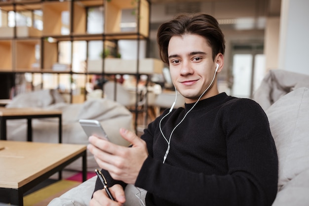 Retrato de estudante feliz na biblioteca conversando por telefone enquanto ouve música.