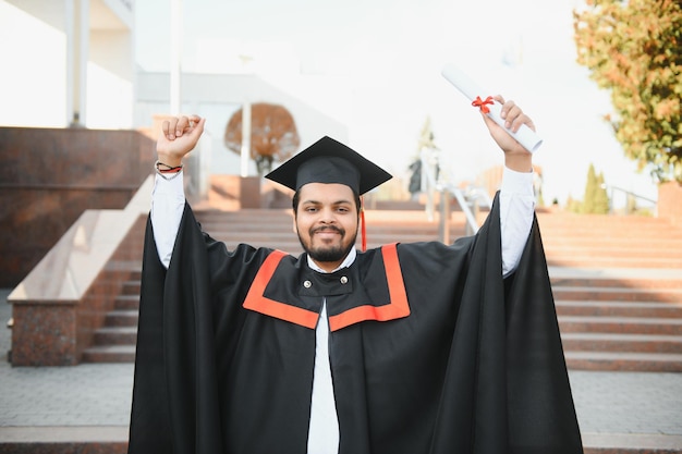 Retrato de estudante indiano bem sucedido em vestido de formatura polegar para cima