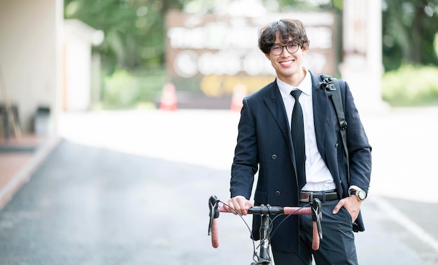 Retrato de estudante universitário sorridente masculino com bicicleta em pé ao ar livre, sorrindo e olhando para a câmera.