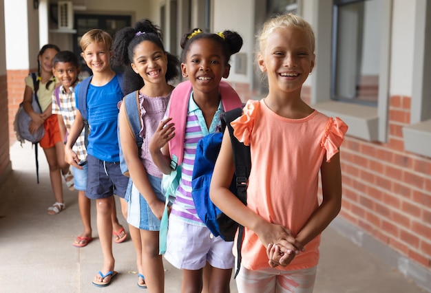 Retrato de estudantes de escola primária multirraciais sorridente com mochila em fila na escola