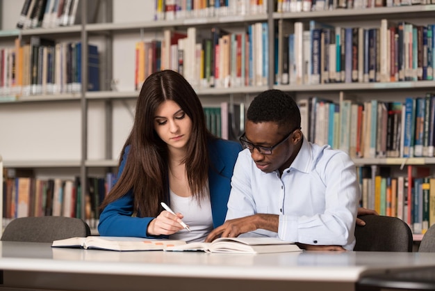 Retrato de estudantes inteligentes com livro aberto lendo na biblioteca da faculdade profundidade de campo rasa