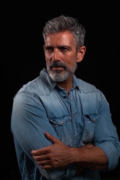 Retrato de estúdio com fundo preto. Foto de meio corpo de um homem caucasiano com cabelos grisalhos na casa dos 50 anos olhando para a câmera