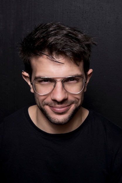 Retrato de estúdio de close-up de jovem homem branco sorrindo com óculos. Ele veste uma camisa preta