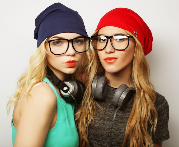 Retrato de estúdio de estilo de vida de garotas hipster de dois melhores amigos vestindo elegantes roupas brilhantes, chapéus, shorts jeans e óculos, enlouquecendo e se divertindo muito juntos. Jovem e bela.