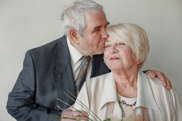 Retrato de estúdio de feliz casal de idosos, abraçando-se contra uma parede cinza.