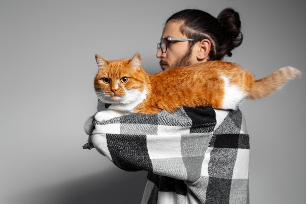 Retrato de estúdio de gato vermelho branco deitado no braço masculino em fundo cinza