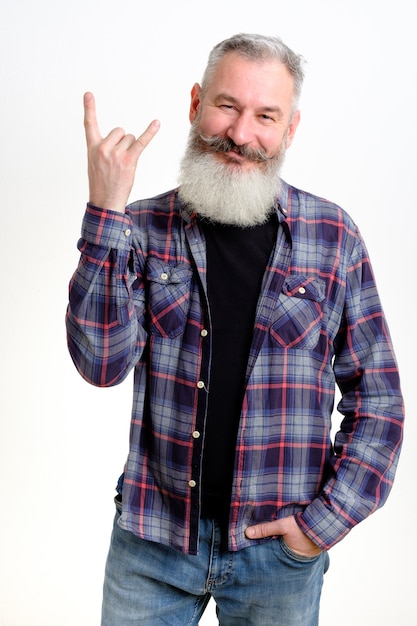 Retrato de estúdio de homem barbudo maduro em roupas casuais mostrando chifres em gesto