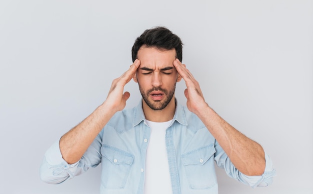 Foto retrato de estúdio de infeliz estudante do sexo masculino caucasiano em pé com os olhos fechados, segurando as mãos na cabeça, parecendo estressante homem estressado, sofrendo de dor de cabeça pessoas tensão de saúde e conceito de enxaqueca