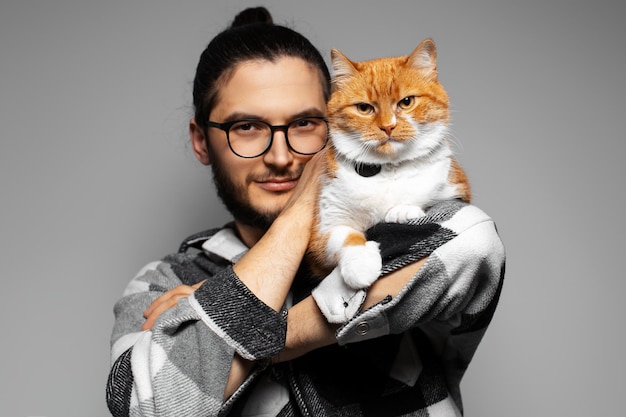 Retrato de estúdio de jovem com gato vermelho no ombro Fundo cinza