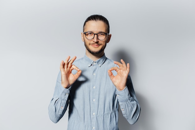 Retrato de estúdio de jovem confiante mostrando o gesto okey no fundo branco