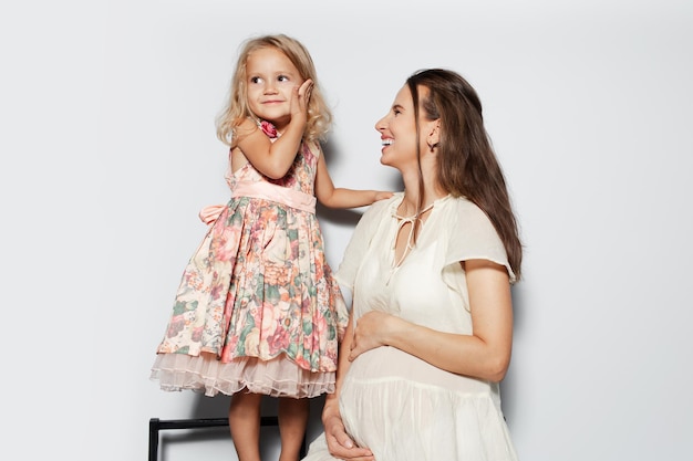 Retrato de estúdio de jovem felicidade grávida e mãe com sua filha em fundo branco