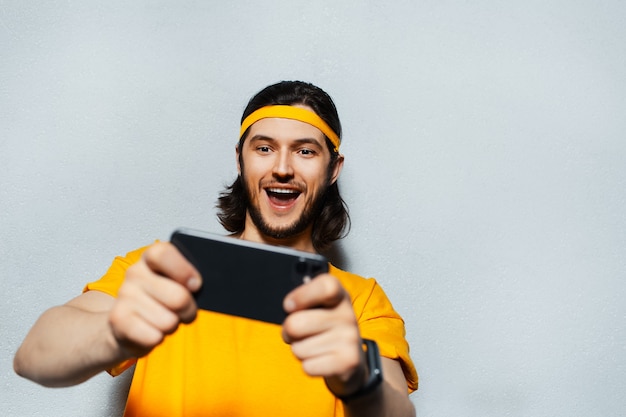 Retrato de estúdio de jovem felicidade usando smartphone em plano de fundo texturizado cinza usando faixa amarela para cabeça e camisa.