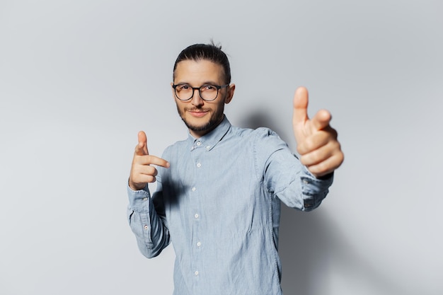 Retrato de estúdio de jovem feliz apontando o dedo em você para a câmera no fundo da cor branca vestindo camisa azul e óculos