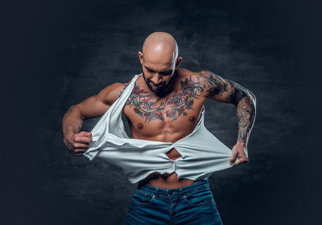 Foto retrato de estúdio de macho atlético com uma tatuagem no peito rasgando a camiseta.