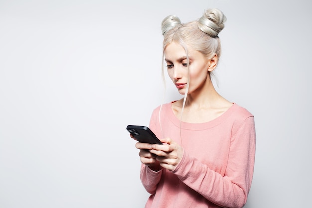 Retrato de estúdio de menina bonita com pães de cabelo olhando no smartphone em branco