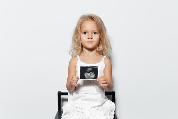 Retrato de estúdio de menina criança com cabelo loiro segurando ultra-som em fundo branco