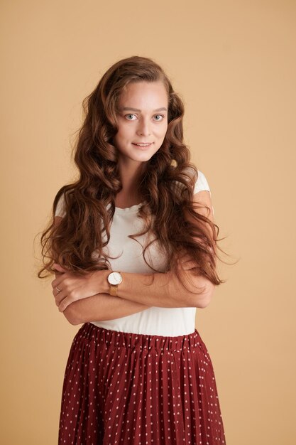 Foto retrato de estúdio de menina sorridente com cabelo encaracolado castanho claro cruzando os braços e olhando para a câmera