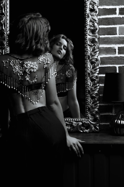 Retrato de estúdio de mulher morena sensual olha para seu reflexo no espelho. Tonalidade em preto e branco