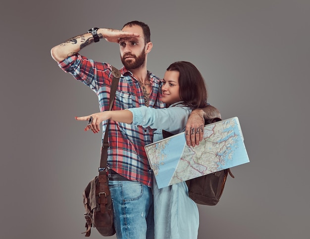 Retrato de estúdio de turistas masculinos e femininos com mochila e mapa, abraçando em um estúdio. Isolado em um fundo cinza.