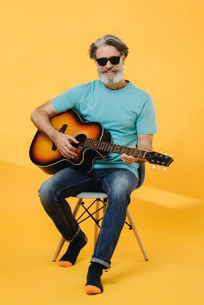 Retrato de estúdio de um homem grisalho idoso em óculos de sol tocando guitarra