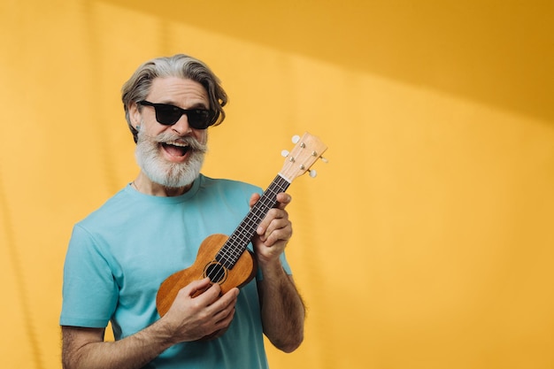 Retrato de estúdio de um homem idoso em óculos de sol tocando um ukulele