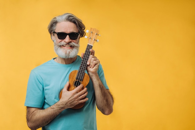 Retrato de estúdio de um homem idoso em óculos de sol tocando um ukulele