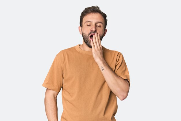Retrato de estúdio de um jovem hispânico bocejando mostrando um gesto cansado cobrindo a boca com a mão