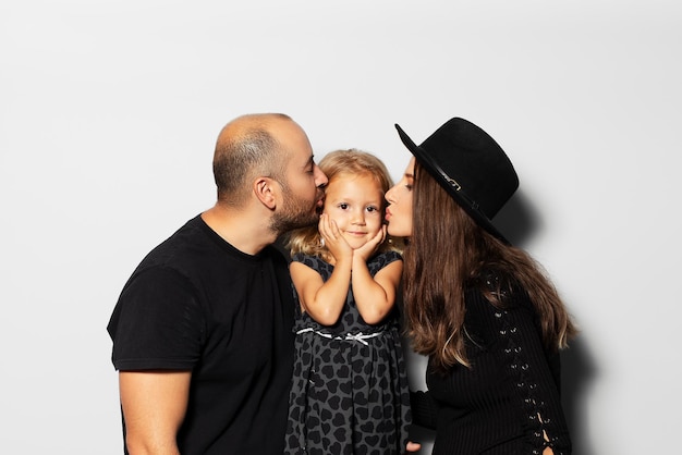 Retrato de estúdio de um jovem pai de família feliz e mãe grávida beija sua filha em fundo branco usando chapéu vestido de preto