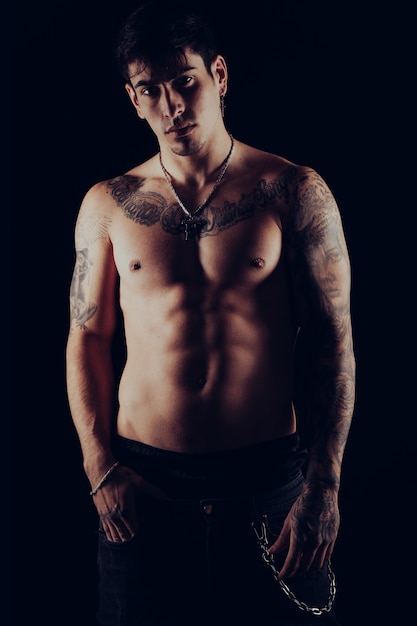 Retrato de estúdio de um jovem sem camisa com tatuagens em pé com uma atitude rude.