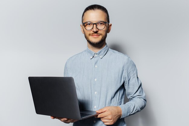 Retrato de estúdio de um jovem sério segurando um laptop nas mãos vestindo camisa azul e óculos em fundo branco